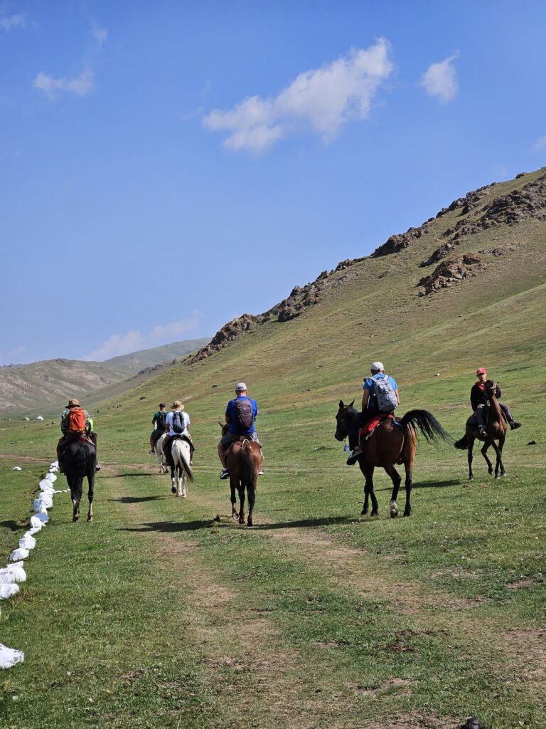 Група туристи на конна езда сред зелените планини на Киргизстан по време на организирана екскурзия от Lemon Tours